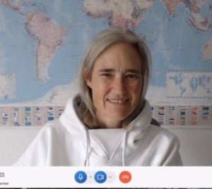 Nina Buschmann at her desk teaching online in front of world map